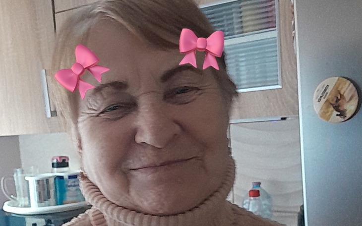 Uśmiechnięta starsza kobieta z różowymi kokardkami na głowie.