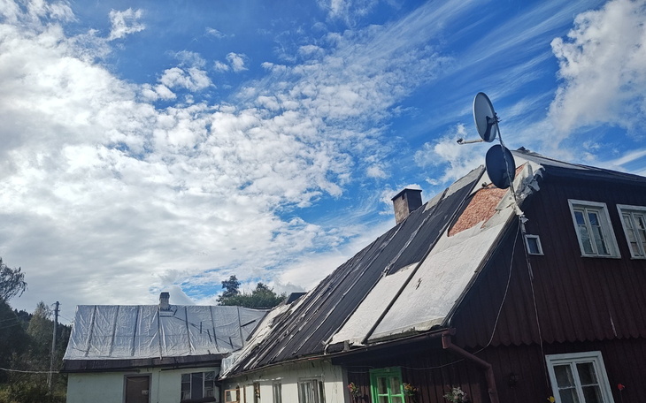 Dom z dachową instalacją solarno-satelitarną pod błękitnym niebem z chmurami.