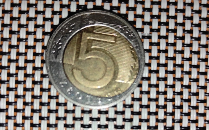 Moneta o nominale 5 zł na tle wzorzystego materiału.