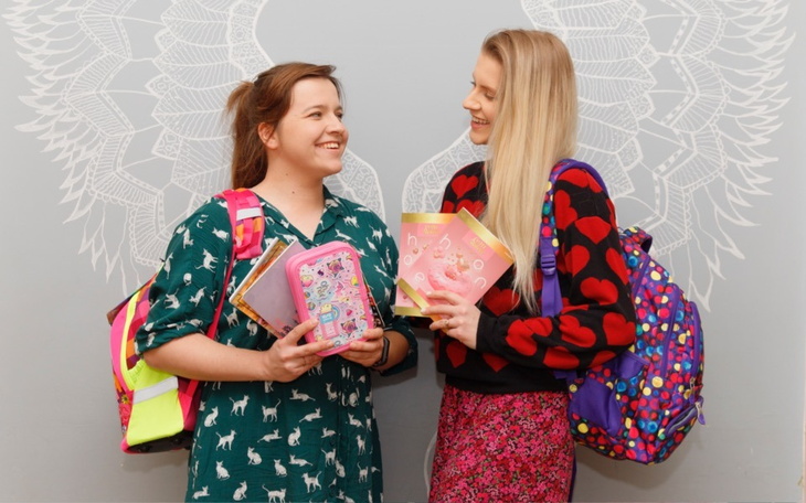 Dwie dziewczyny uśmiechające się, trzymające zeszyty i plecaki.