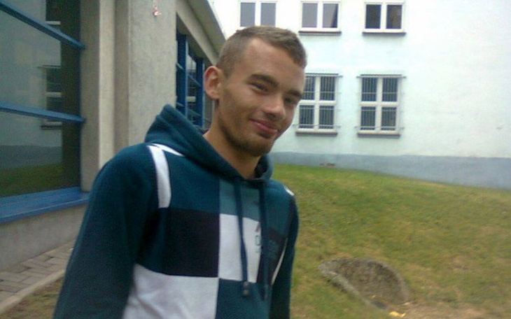 Młody mężczyzna uśmiechający się na tle budynku.