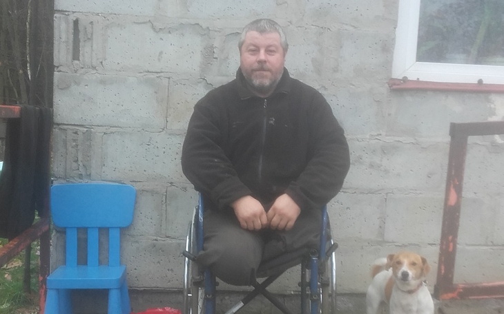 Mężczyzna na wózku inwalidzkim siedzi obok psa w otoczeniu budynku.