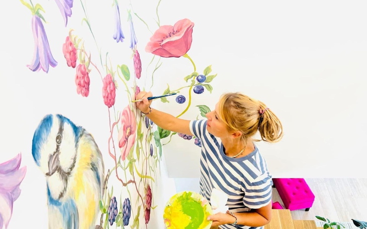 Artystka malująca mural z kolorowymi kwiatami i ptakami.
