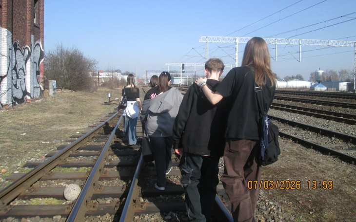 Grupa ludzi spacerujących po torach kolejowych.