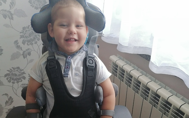 Uśmiechnięty chłopiec w foteliku, siedzący przy oknie.