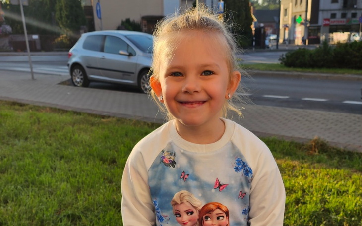 Uśmiechnięta dziewczynka w bluzie z postaciami z bajek.