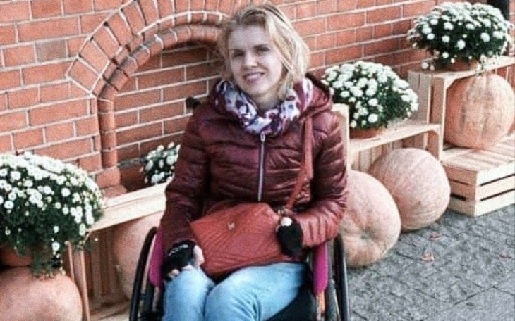 Kobieta na wózku inwalidzkim w otoczeniu dyni i kwiatów.