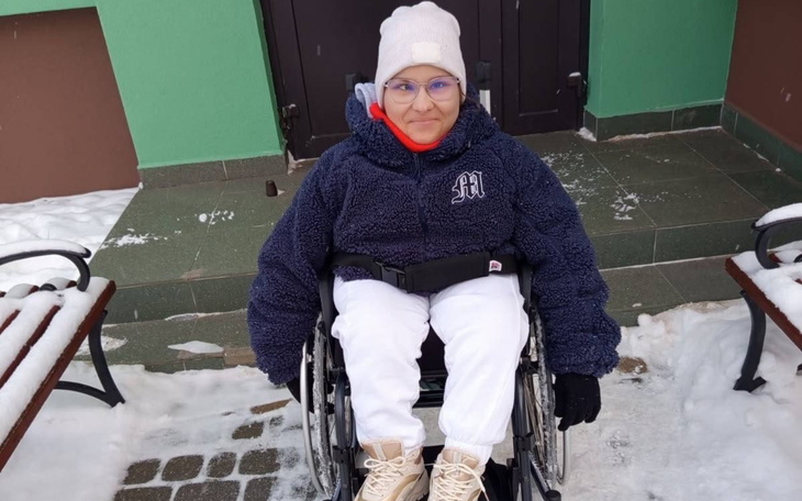 Młoda dziewczyna w wózku inwalidzkim na tle zielonej ściany.