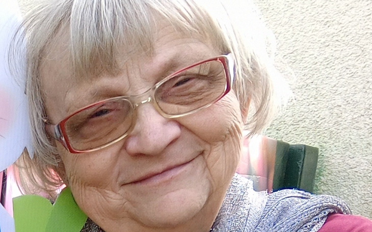 Uśmiechnięta starsza kobieta z okularami, w otoczeniu kwiatów.