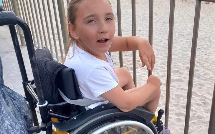 Dziewczynka w wózku inwalidzkim, uśmiechająca się na placu zabaw.