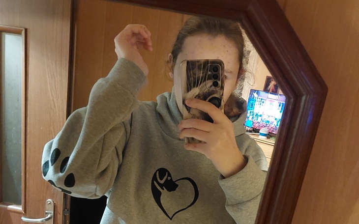 Osoba w szarej bluzie robiąca selfie w lustrze.