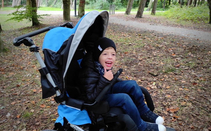 Chłopiec w wózku spacerowym, uśmiechający się do kamery.