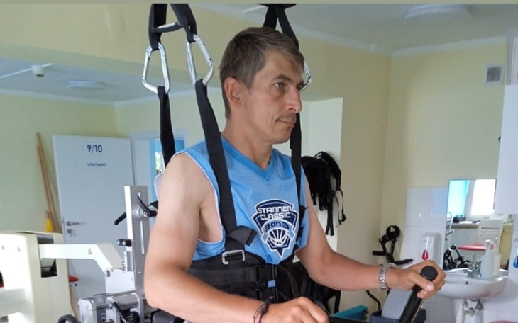 Mężczyzna w sprzęcie rehabilitacyjnym, ćwiczący w sali.