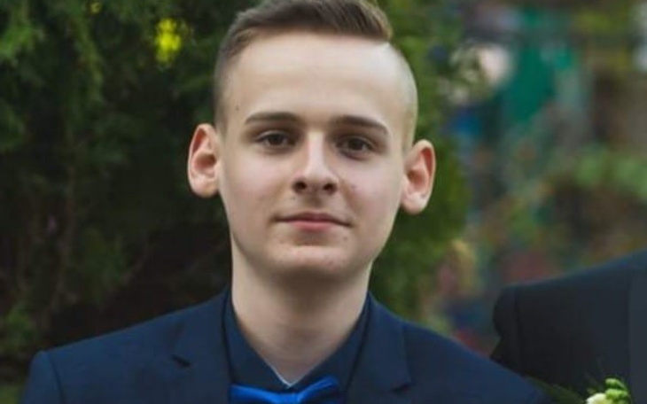 Młody mężczyzna w eleganckim garniturze, z poważnym wyrazem twarzy.