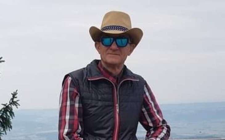 Mężczyzna w kapeluszu i okularach przeciwsłonecznych, pozujący na tle krajobrazu.