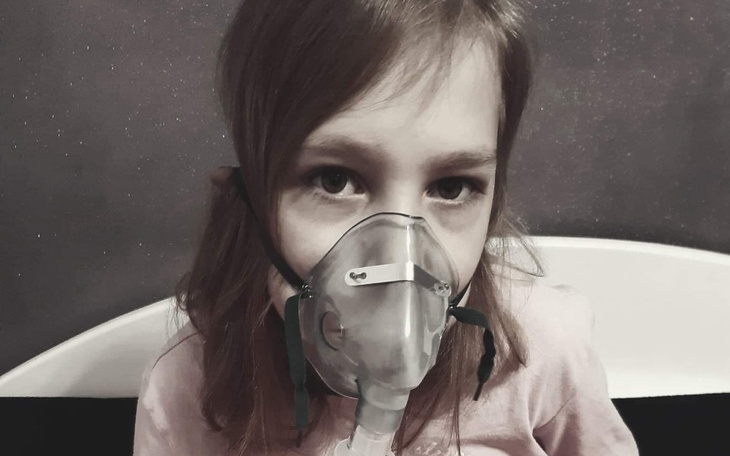 Dziewczynka z maską tlenową, wyraz troski na twarzy.
