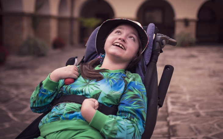 Dziewczynka w wózku, uśmiechająca się w słonecznym otoczeniu.