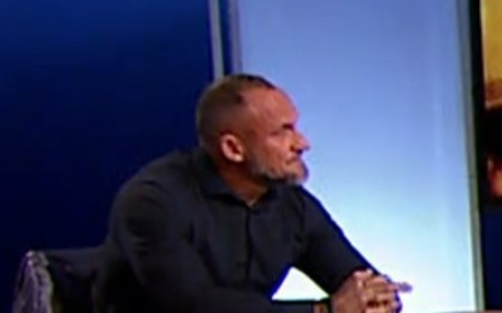 Mężczyzna w czarnej koszuli, siedzący przy stole, z zamyśloną miną.