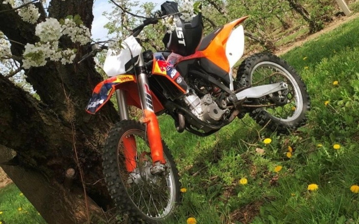 Motocykl terenowy oparty o drzewo w kwitnącym otoczeniu.