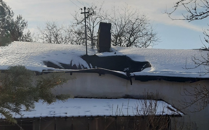 Uszkodzony dach budynku pokryty śniegiem, z widocznym kominem.