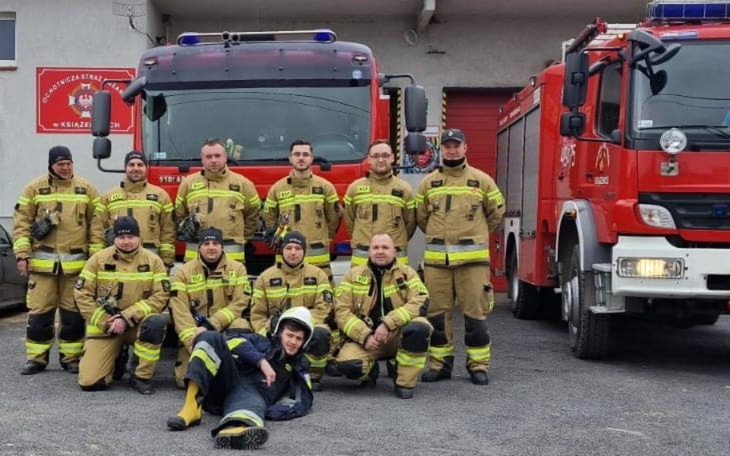 Grupa strażaków w mundurach przed wozem strażackim.
