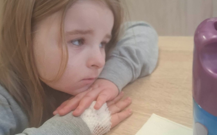 Dziewczynka smutno patrzy w dal, opierając głowę na dłoni.