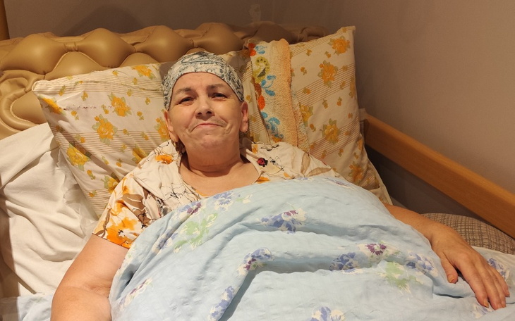 Starsza kobieta w łóżku, uśmiechająca się do kamery.