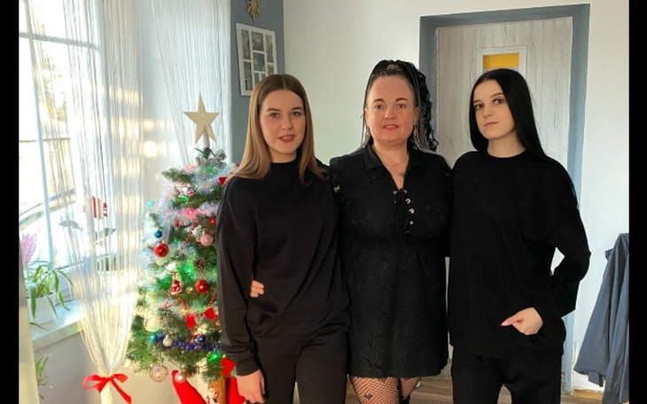 Trzy osoby w czarnych ubraniach pozujące przy choince.