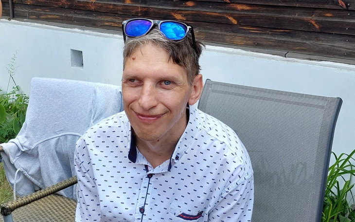 Mężczyzna w okularach przeciwsłonecznych, uśmiechający się na zewnątrz.