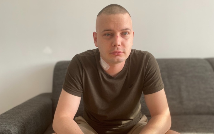 Mężczyzna siedzący na kanapie, z widoczną blizną na szyi.