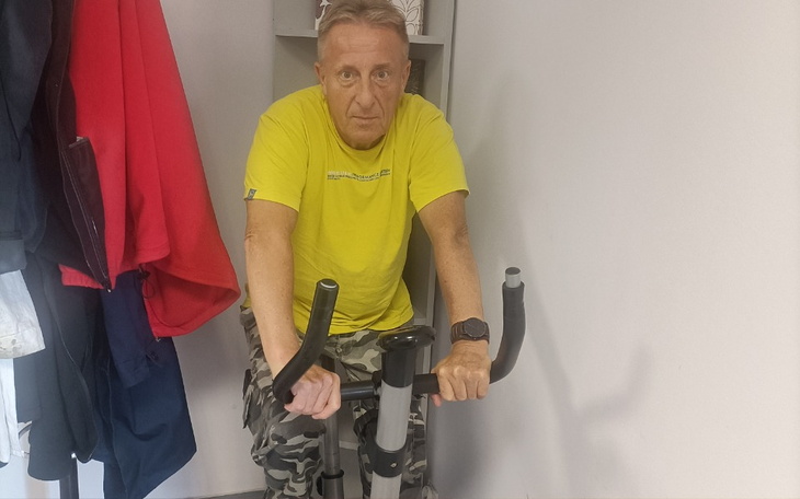 Mężczyzna w żółtej koszulce na rowerze stacjonarnym, skupiony na treningu.