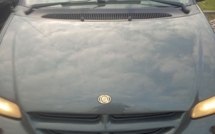 Widok na maskę samochodu z odbiciem chmur.