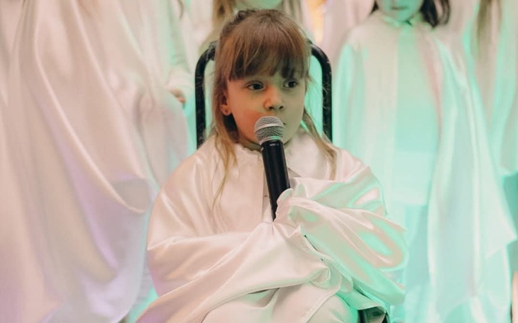 Dziewczynka w białym stroju, trzymająca mikrofon.