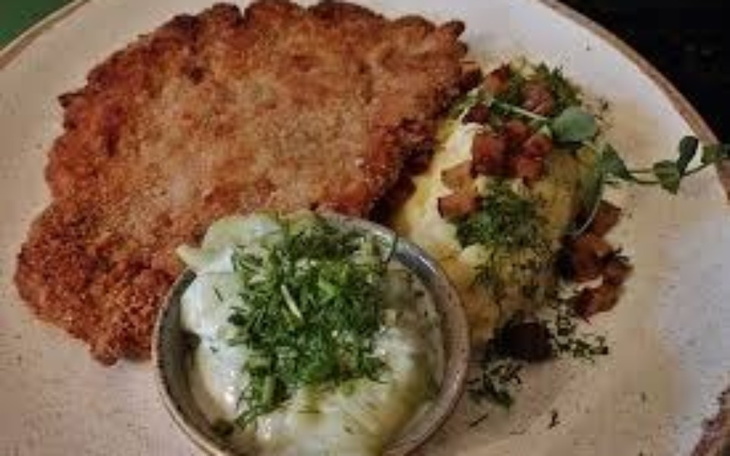 Talerz z kotletem i dodatkami, podany na talerzu.