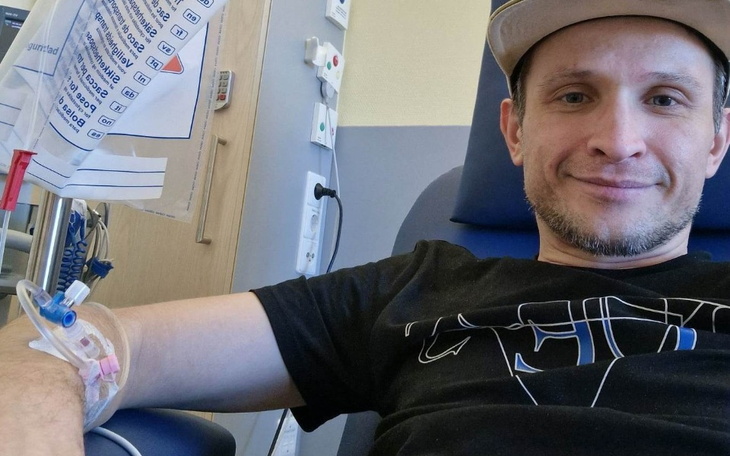 Mężczyzna w szpitalu, z kroplówką i uśmiechem na twarzy.