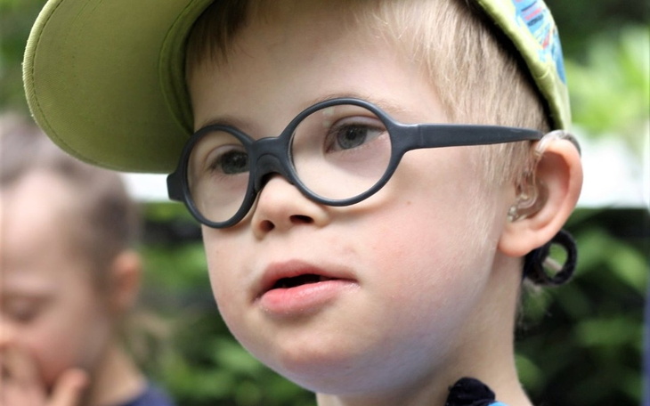 Chłopiec w okularach i czapce, uśmiechający się w otoczeniu zieleni.