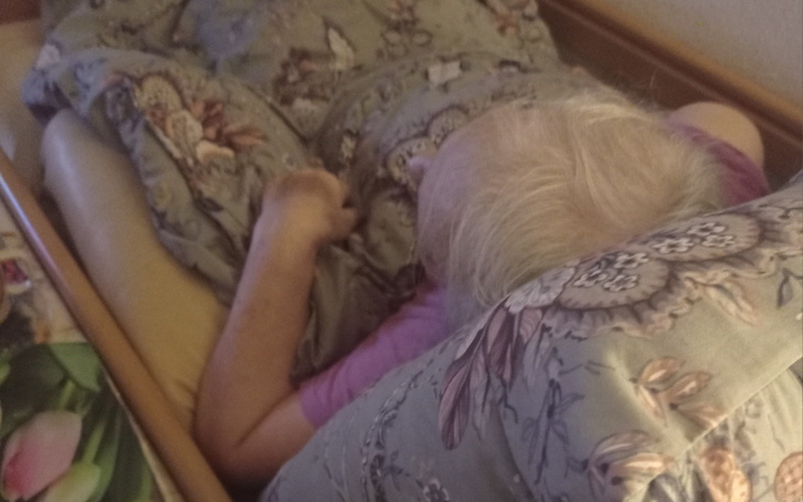 Osoba leżąca w łóżku pod kołdrą, z widoczną ręką.