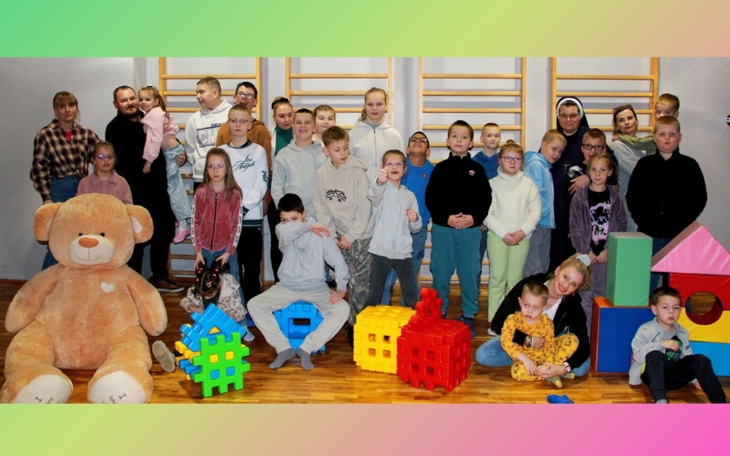 Grupa dzieci bawiących się w sali z kolorowymi zabawkami.