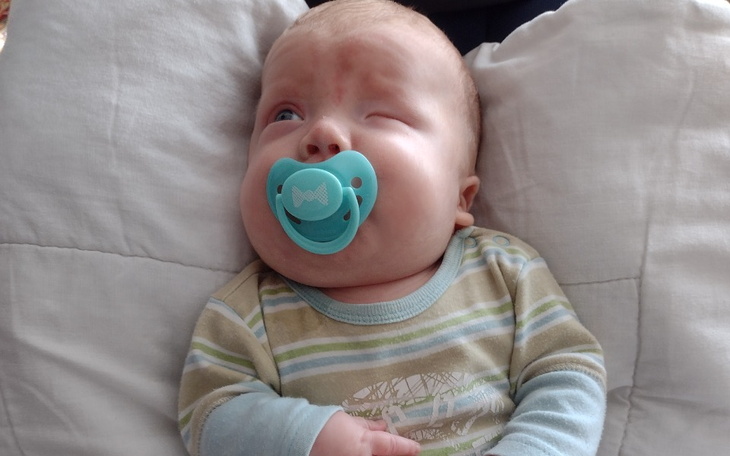 Niemowlę z smoczkiem, leżące na poduszce.