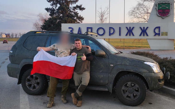 Dwaj mężczyźni z flagą Polski przy samochodzie, w tle znak Zadoriż.