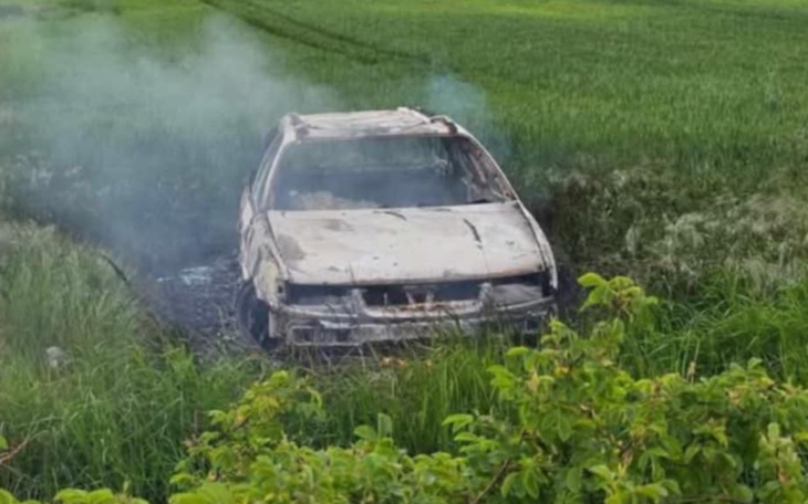 Spalony samochód w zaroślach, wydobywający dym.