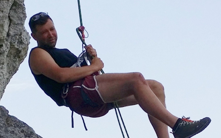 Mężczyzna wspinający się na skałę, z uśmiechem na twarzy.