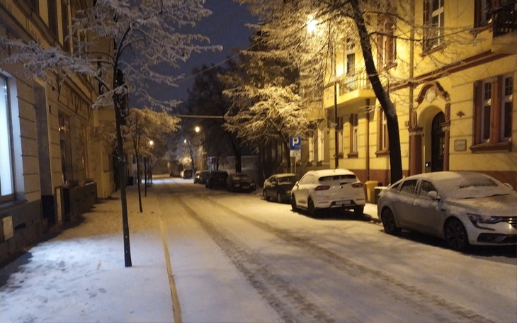 Zimowa ulica pokryta śniegiem w nocy, oświetlona latarniami.