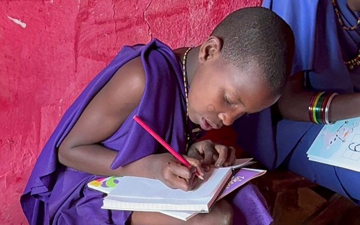 Chłopiec w tradycyjnym stroju, pisze w zeszycie.