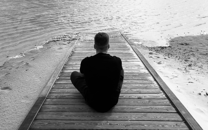 Mężczyzna siedzący na pomoście, patrzący na wodę.