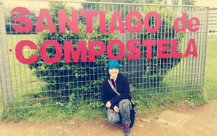 Osoba siedząca przy znaku Santiago de Compostela.