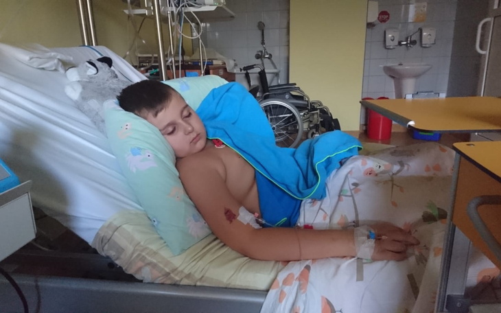 Chłopiec leży w szpitalnym łóżku, przykryty kocem, z kroplówką.