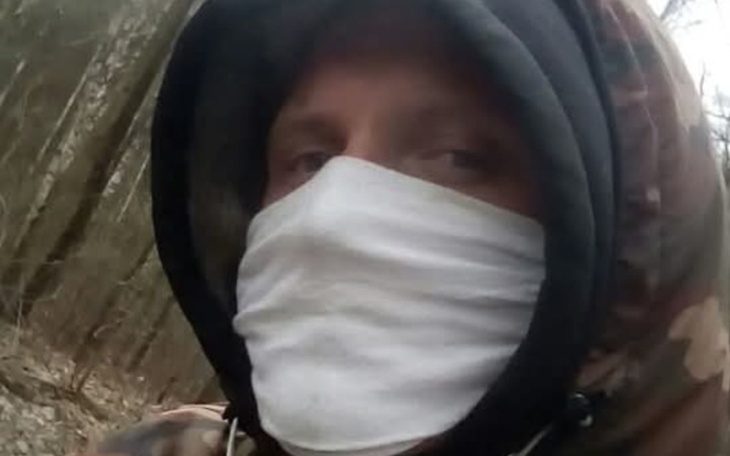 Mężczyzna w masce na tle lasu, ubrany w ciepłą odzież.