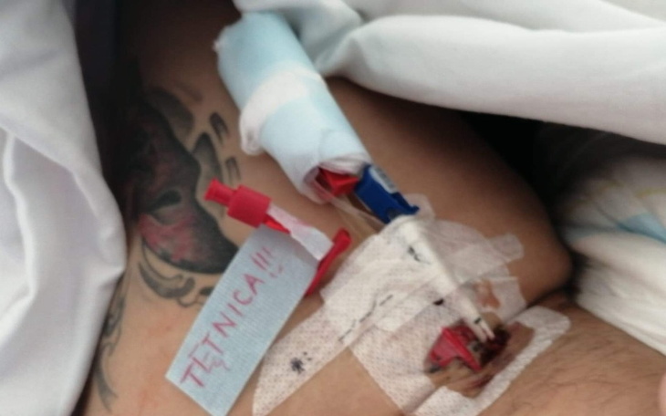 Pacjent z opatrunkiem i cewnikiem, leżący w szpitalnym łóżku.