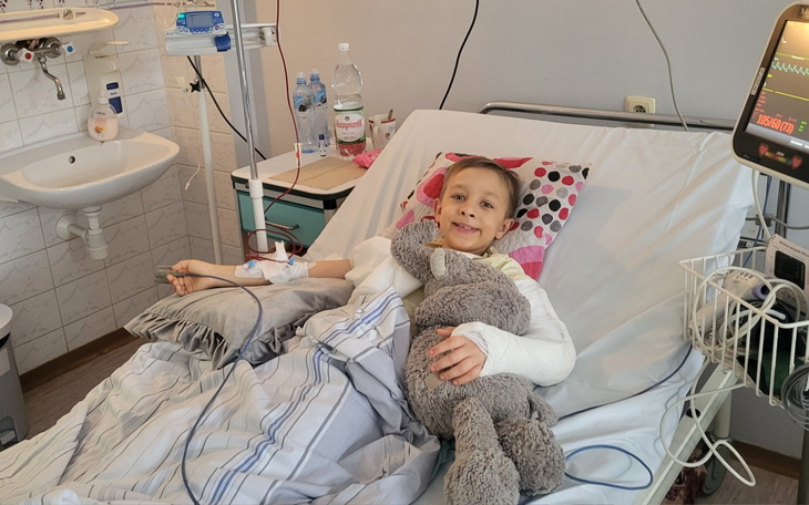 Chłopiec w szpitalu z pluszowym misiem, uśmiechnięty mimo kontuzji.